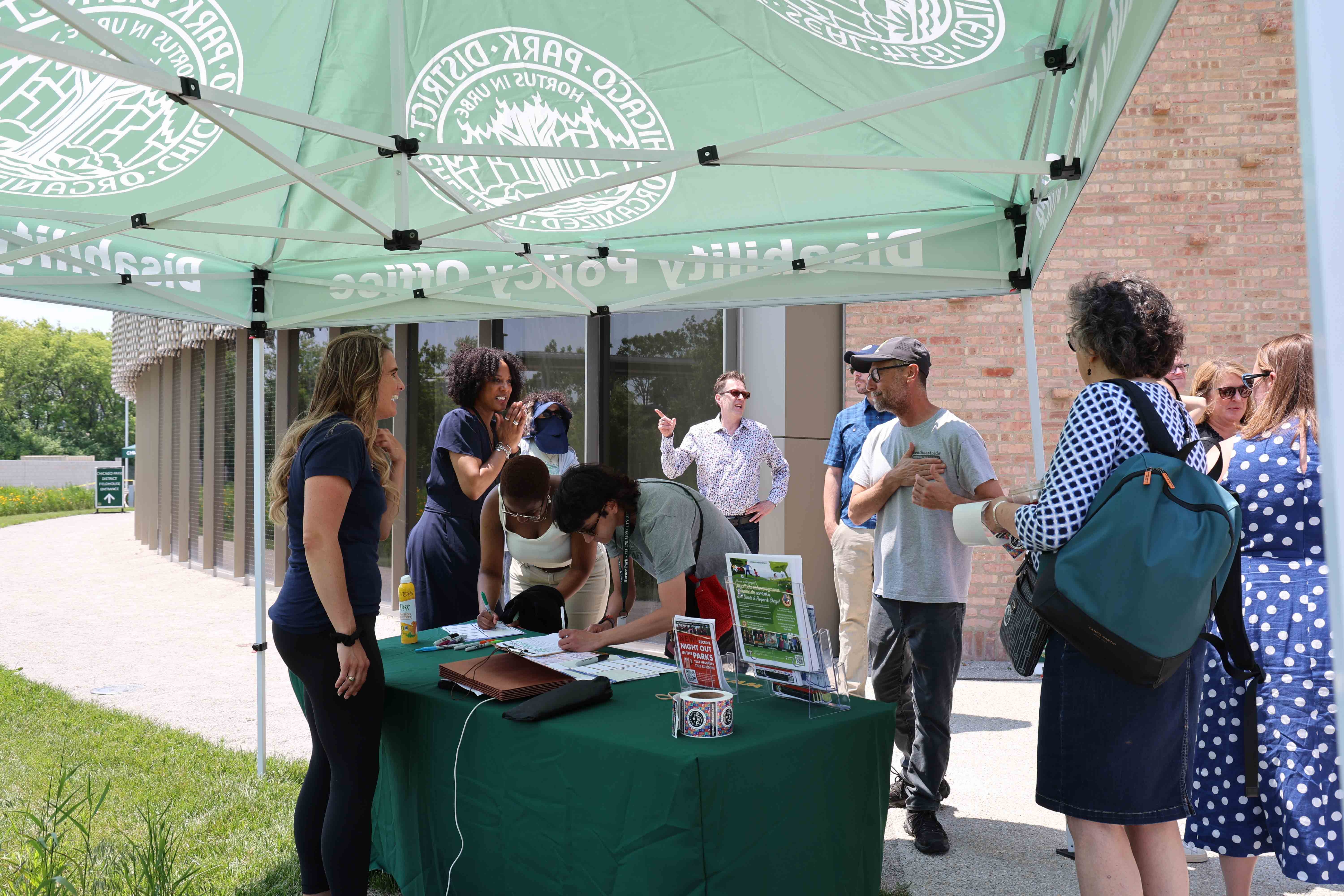 People gather at an information table under a Chicago Park District tent.